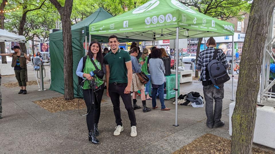 A volunteer in a green vest holds a news microphone beside the tent.