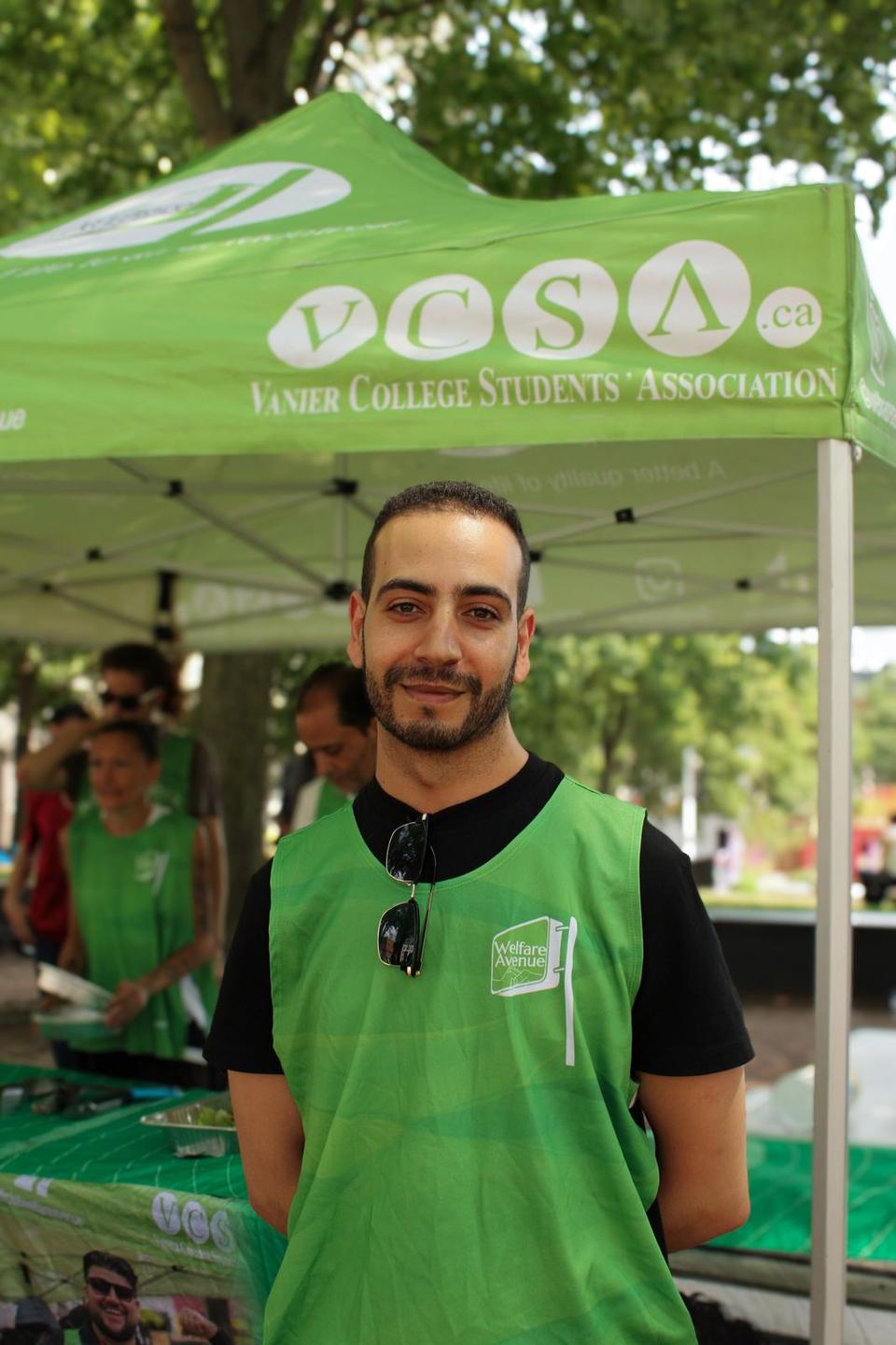 A smiling volunteer in a green Welfare Avenue vest stands at the tent.