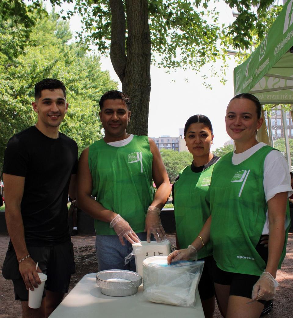 Four smiling volunteers pose at a table of plates, napkins and foil trays.