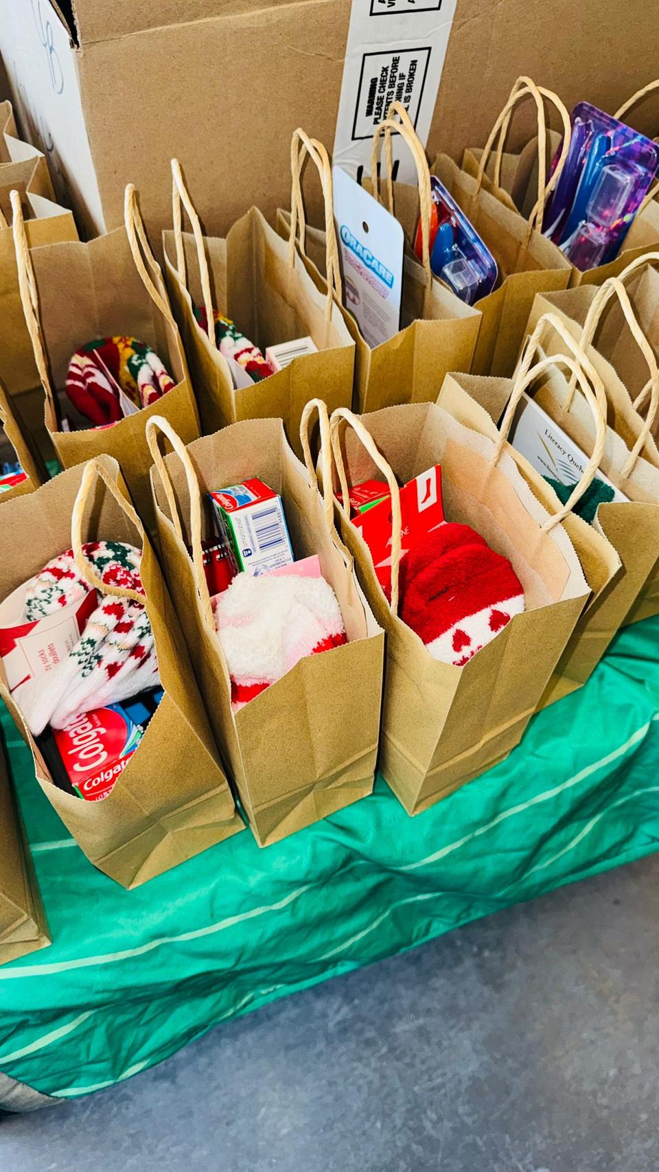 Brown paper gift bags filled with presents line a green table.