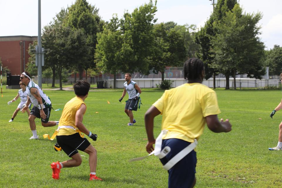 Players in yellow and white chase the play across the field, flags at their hips.