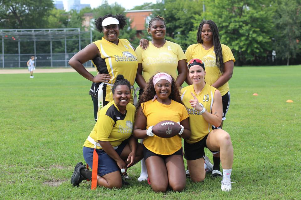 A team in yellow jerseys poses on the grass, the front row kneeling around a football.