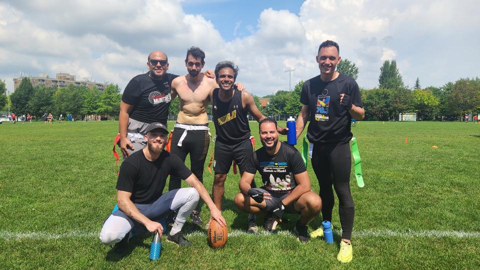 A group of players poses on the field under a blue sky, some crouching in front with a football.
